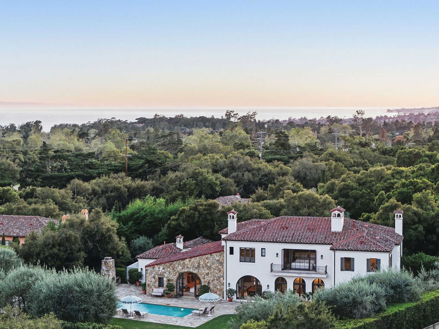 Pool and stone-clad rear elevation looking over treetops to the Pacific