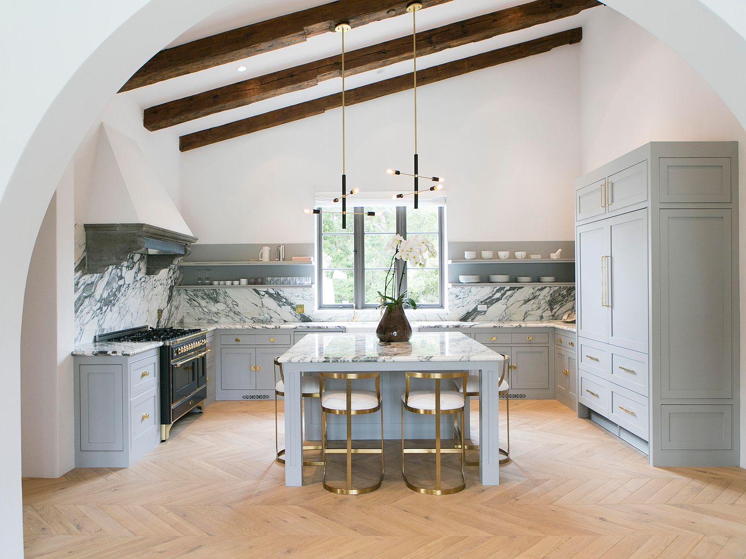 Living room with stone fireplace, beamed ceiling, and chevron oak floor