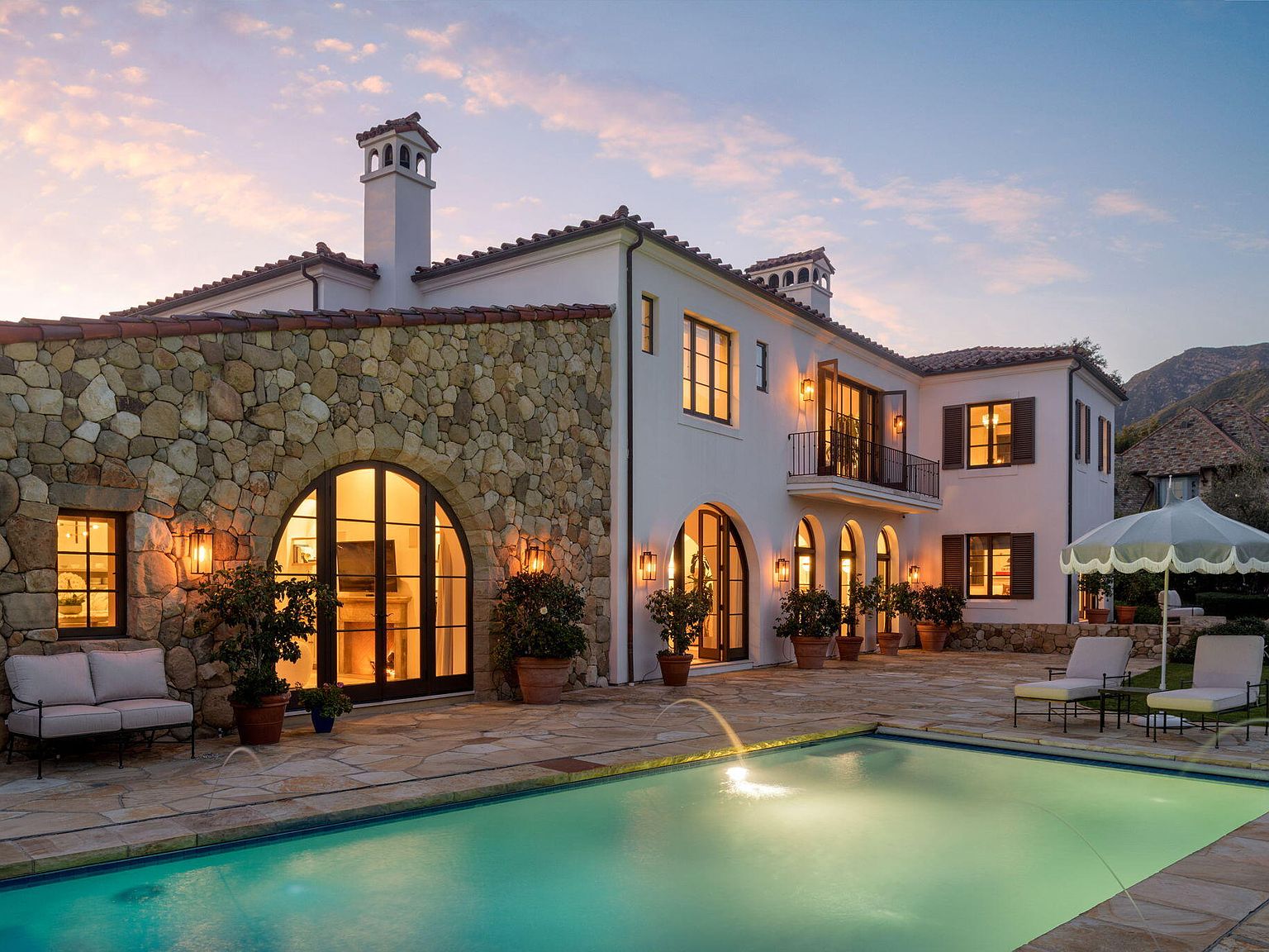 Twilight pool view with stone arches and lit interior windows